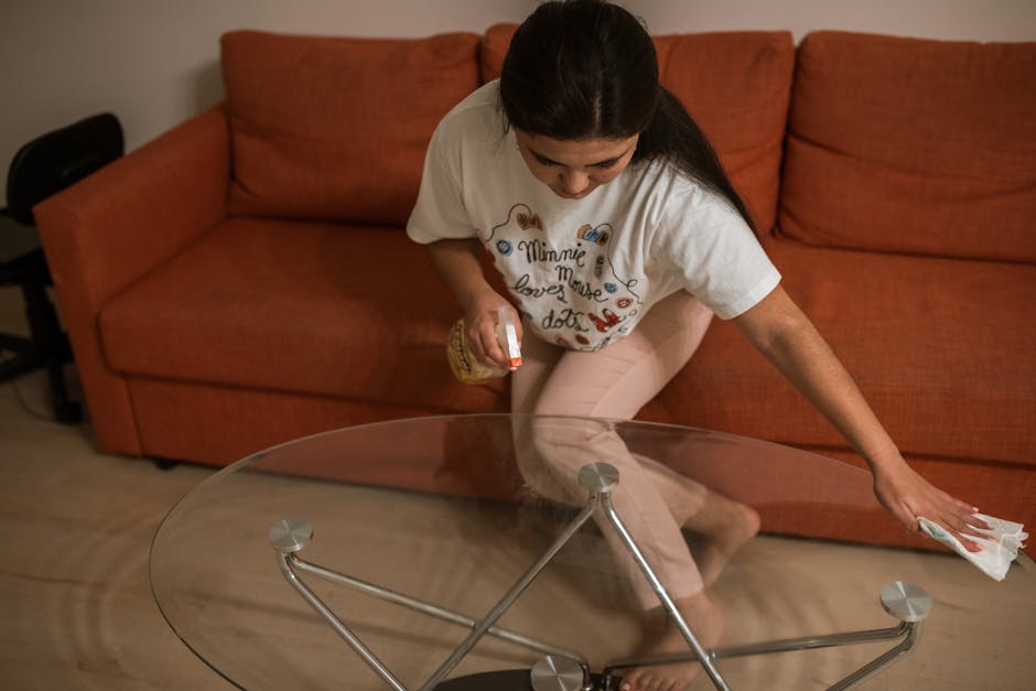 A professional cleaner from Putney Carpet Cleaners, dressed in full protective gear including a white coverall, gloves, mask, and goggles, is performing surface cleaning and sanitisation on a black fa