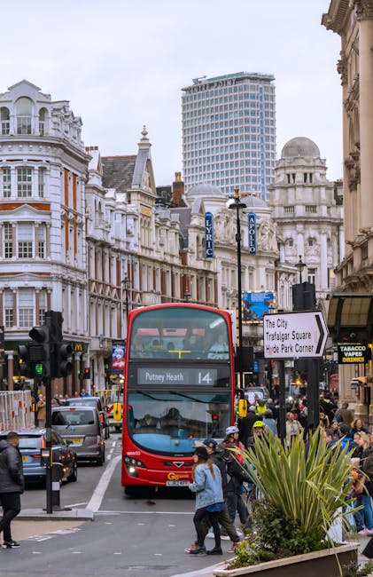 A busy street scene in Putney showing a red double-decker bus marked 'Putney Heath 14' approaching a crosswalk. The street is lined with historic Victorian-style buildings with ornate facades and larg